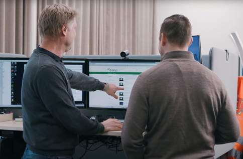 Två personer samarbetar vid flera datorskärmar och analyserar digitala lösningar i modern kontorsmiljö med fokus på affärssystem