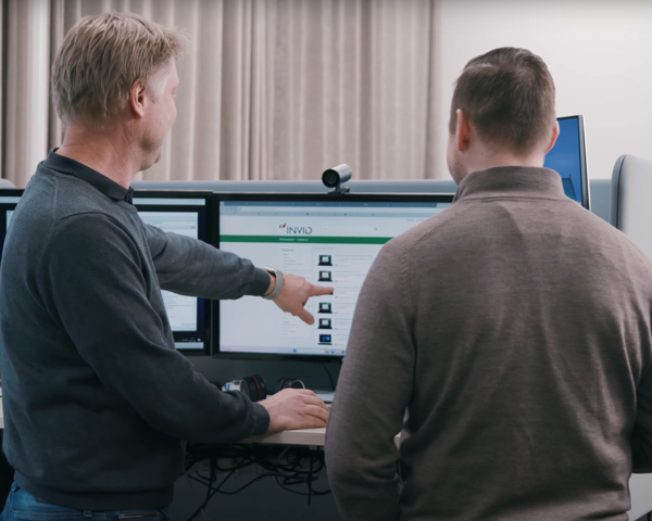 Två personer samarbetar vid flera datorskärmar och analyserar digitala lösningar i modern kontorsmiljö med fokus på affärssystem
