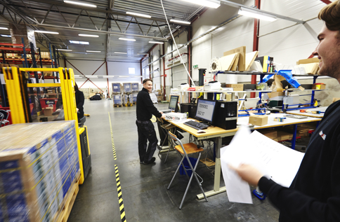 Medarbetare på Electro Elco arbetar i lager- och produktionsmiljö med orderhantering, logistikflöden och kvalitetskontroll vid arbetsstation nära lager och trucktrafik