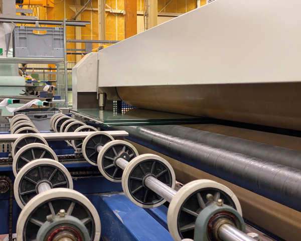 Automatiserad glasbearbetning i produktionslinje där glasrutor transporteras genom industriell maskinutrustning för tillverkning och förädling
