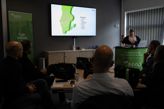 Mötesdeltagare lyssnar på presentation med karta på skärm, Anne-Marie Achrenius vid podium i konferensrum med INVID-profilering