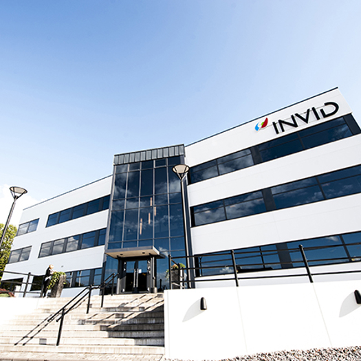 Modern kontorsbyggnad med glasentré och trappa, med INVID-logotyp på fasaden under klar blå himmel