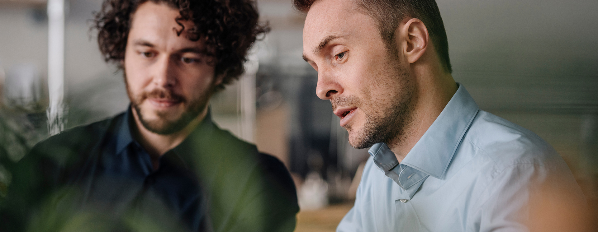 Två kollegor sitter tillsammans i kontorsmiljö och diskuterar arbete vid dator, vilket visar IT‑konsultation på plats, samarbete, rådgivning och genomgång av digitala lösningar i verksamheten