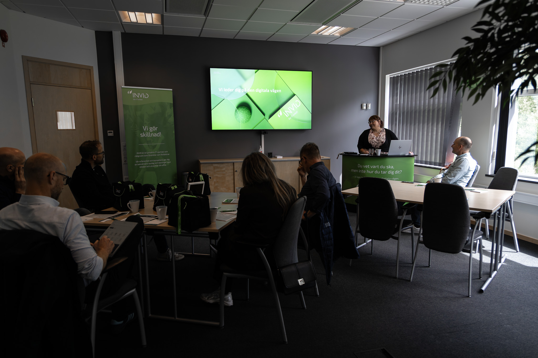 Mötesrum på INVID med presentation om digitala verktyg där deltagare sitter vid bord och lyssnar på föreläsare vid skärm