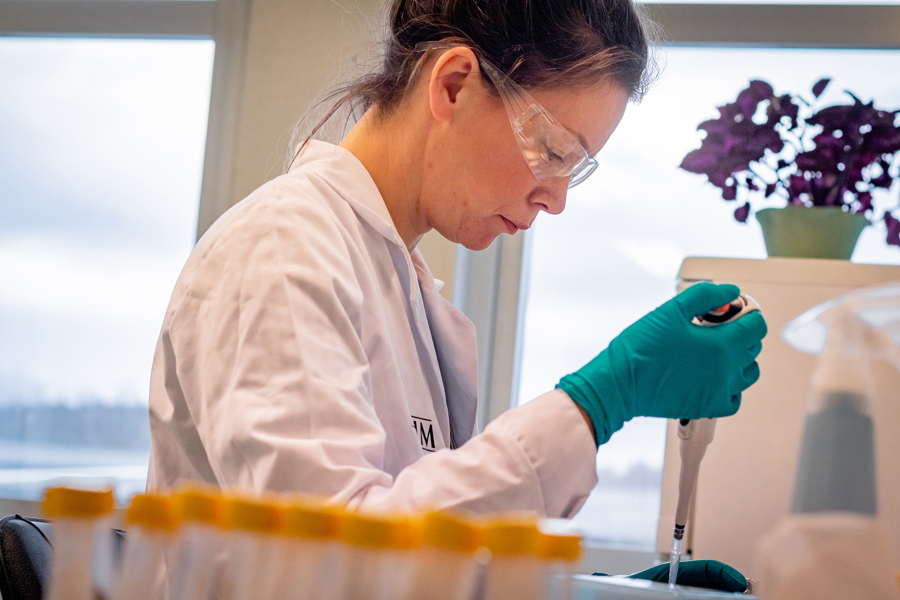 Person arbetar i laboratorium med pipett, skyddsglasögon och provrör för analys, kvalitetskontroll och kemisk forskning