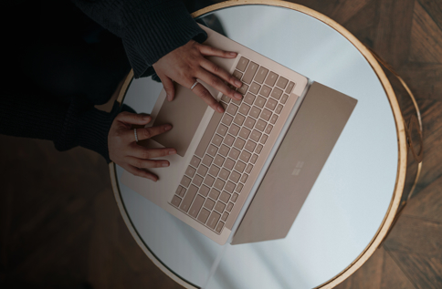Närbild ovanifrån på person som arbetar vid laptop på runt bord, där tangentbord och händer syns tydligt, vilket visar digitalt arbete, produktivitet och användning av Microsoft 365 i modern arbetsmiljö