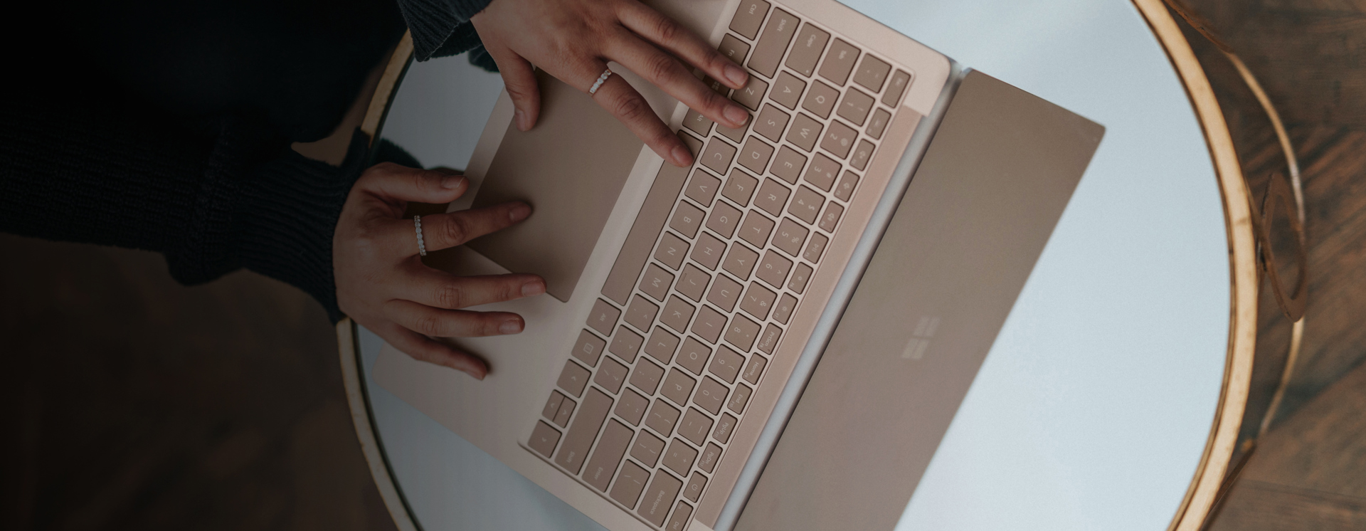 Närbild ovanifrån på person som arbetar vid laptop på runt bord, där tangentbord och händer syns tydligt, vilket visar digitalt arbete, produktivitet och användning av Microsoft 365 i modern arbetsmiljö