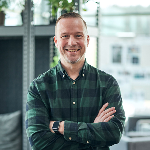 Porträttbild av medarbetare i kontorsmiljö med korsade armar framför fönster, använd för presentation av kontaktperson eller expert