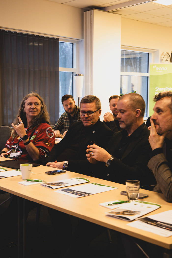Flera personer sitter vid ett bord i ett konferensrum under ett seminarium, med anteckningar, glas och kaffekoppar framför sig, medan en INVID‑rollup syns i bakgrunden