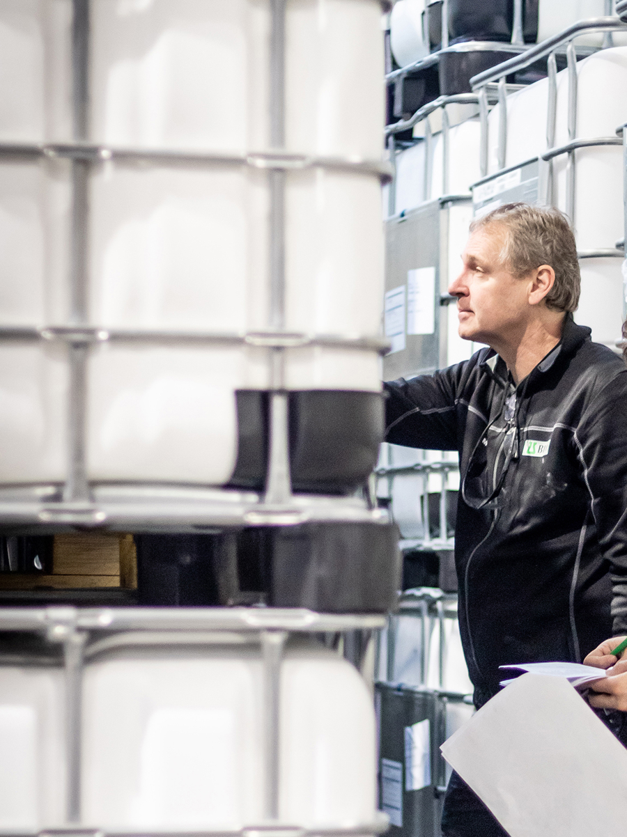 Medarbetare på BIM Kemi arbetar med lagerhantering och kvalitetskontroll bland kemikaliebehållare i produktionsmiljö med fokus på logistik och säkerhet