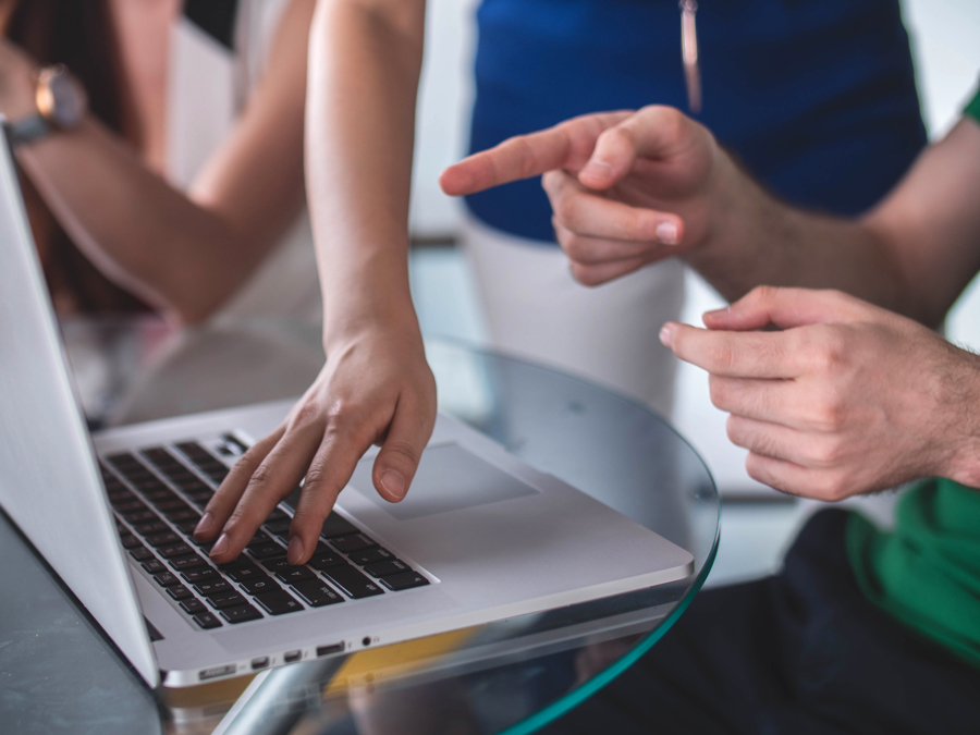 Närbild av två personer som samarbetar vid laptop där en person skriver på tangentbordet och en annan pekar på skärmen, vilket visar samarbete, support och arbete i Microsoft 365 och digitala arbetsprocesser