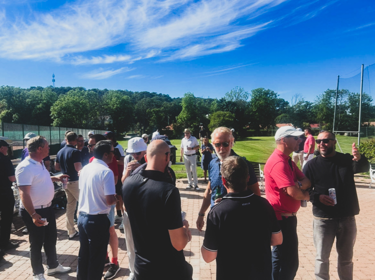 Deltagare minglar och nätverkar utomhus vid golfevent på solig terrass med utsikt över golfbanan