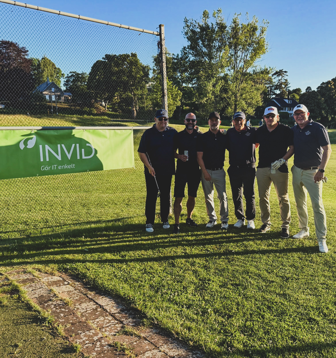 Gruppbild Från Företagsgolf Där Deltagare Poserar Framför INVID Banner På Golfbanan I Kvällssol