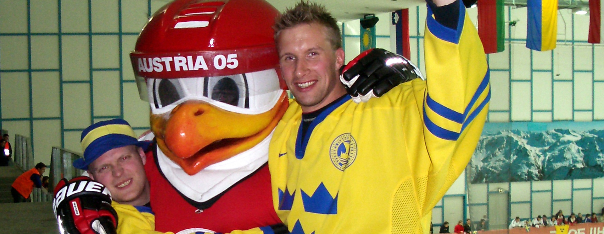 Tre personer i gula hockeytröjor firar tillsammans med en maskot i en ishall