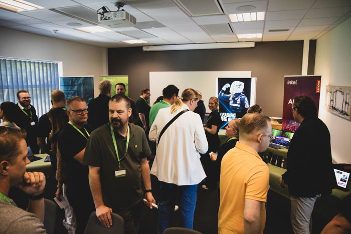 Deltagare minglar och testar teknik vid demo-stationer inomhus under event, med utställning från olika leverantörer och skärmar i bakgrunden.