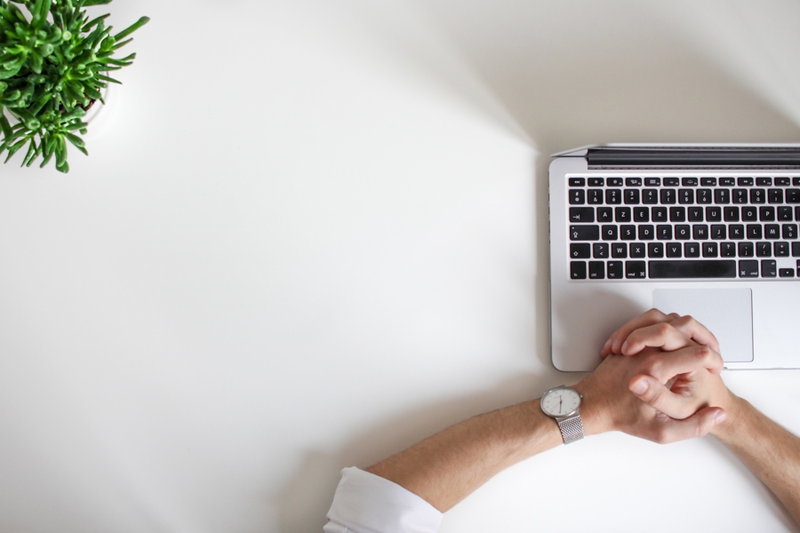 Minimalistisk arbetsyta med laptop på skrivbord där händer vilar framför tangentbordet, tillsammans med växt och vit bakgrund som visar digitalt arbete, fokus och effektiv användning av Microsoft 365 i modern arbetsmiljö