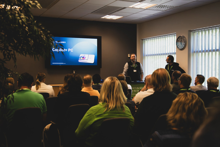 Föreläsning om Copilot+ PC inför publik i konferensrum, med presentation på skärm och deltagare sittande i rader.