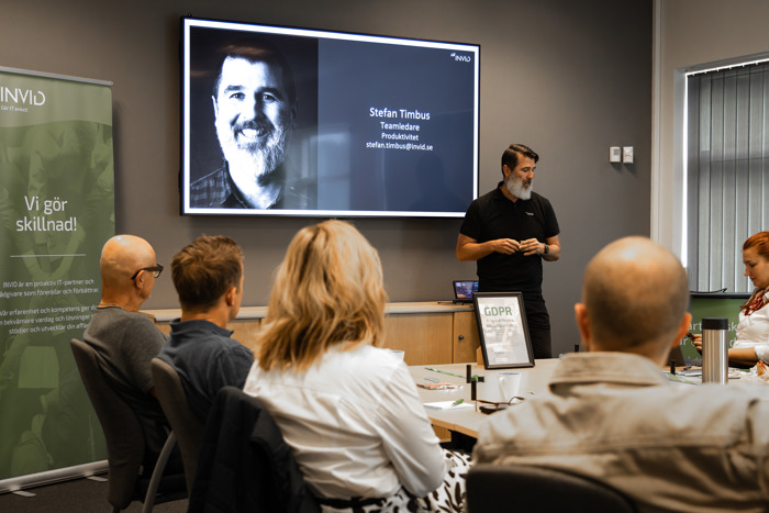 Presentatör står framför skärm under nätverksmöte, deltagare sitter vid konferensbord