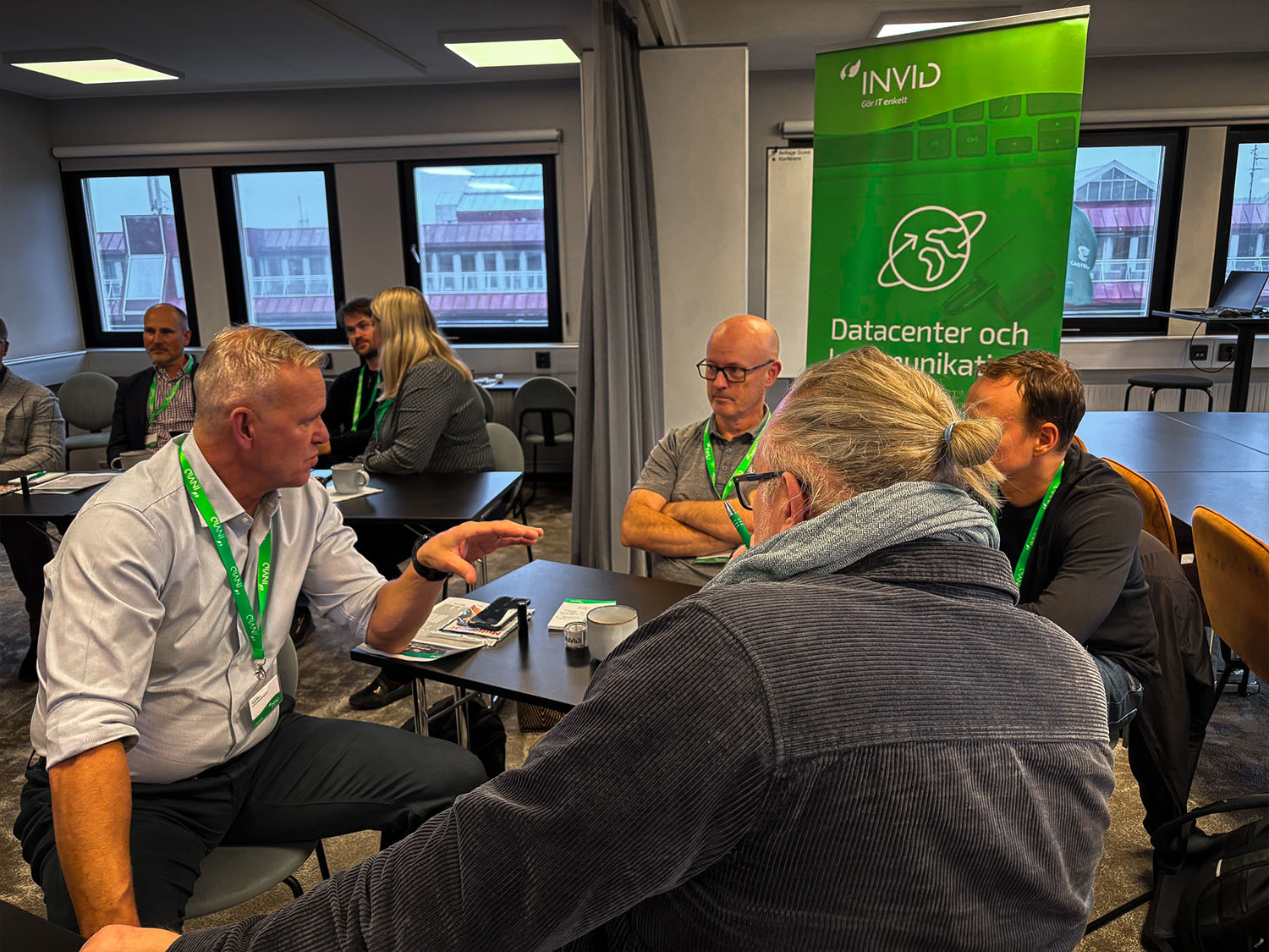 Deltagare med gröna nyckelband sitter i grupp och diskuterar engagerat under seminariet, med en INVID-banner i bakgrunden.