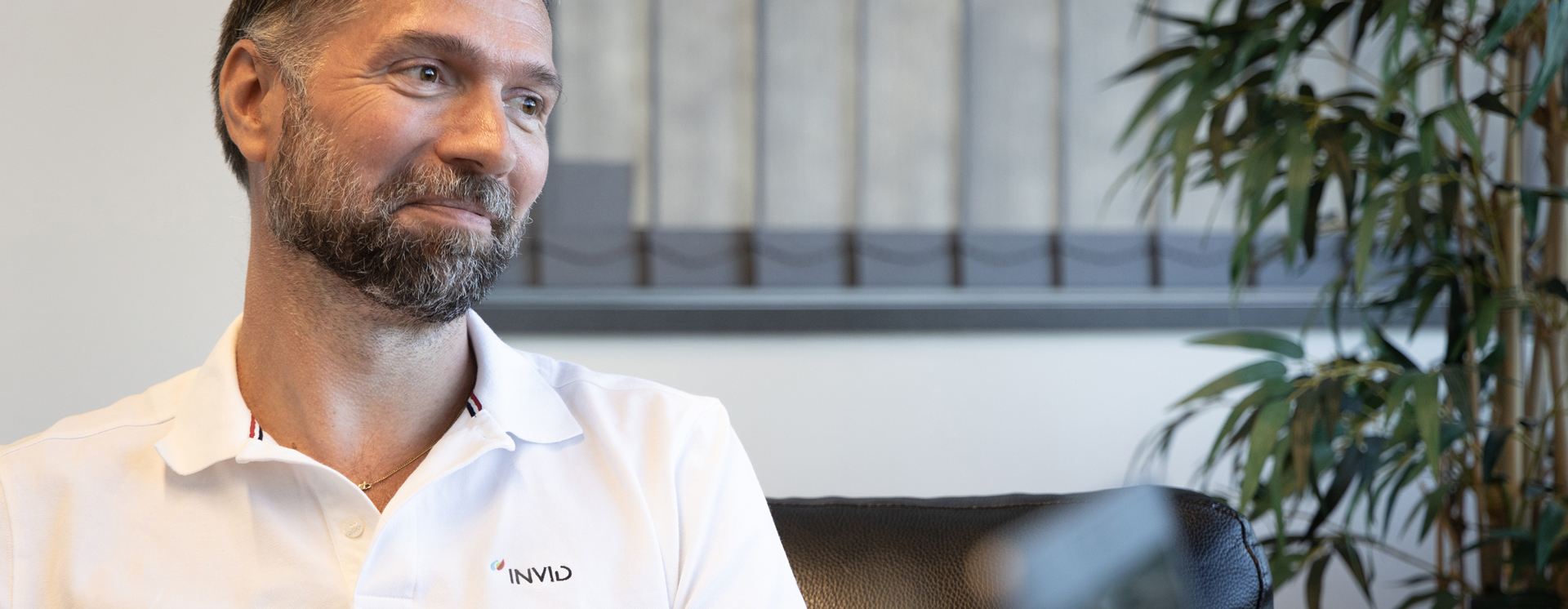 Pierre Lundbgren sitter i en fåtölj i ett kontor och ler, med en annan person suddig i förgrunden samt en stor grön växt och fönster med persienner i bakgrunden
