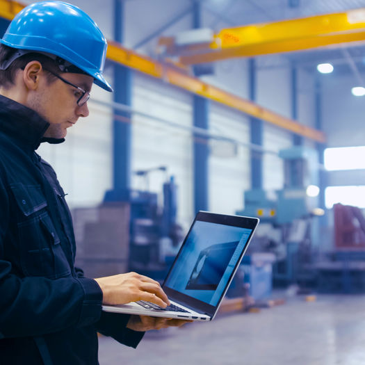 Stock Photo Factory Worker In A Hard Hat Is Using A Laptop Computer With An Engineering Software 702079537