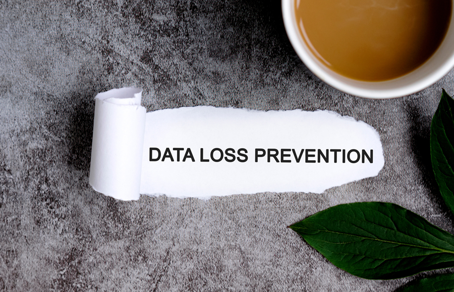 Papper med texten “DATA LOSS PREVENTION” på ett bord, med en kopp kaffe och gröna blad bredvid